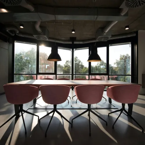 Modern conference room with pink chairs, large windows, pendant lights, and natural light streaming in.