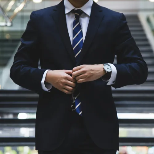 Man in navy suit and striped tie buttoning jacket in front of modern stairway