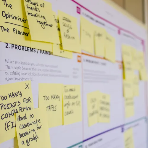 Close-up of a board covered with yellow sticky notes for brainstorming project problems and solutions.