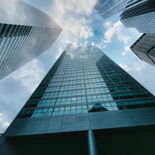 Upward view of tall glass skyscrapers against a cloudy blue sky in a modern cityscape.