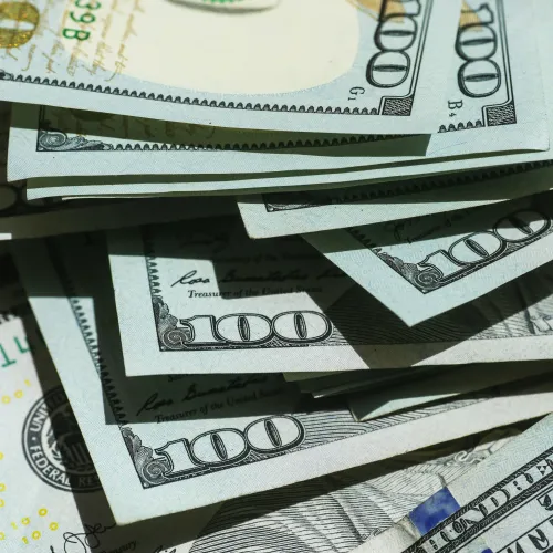 Stack of US one hundred dollar bills showing detailed currency design and security features.