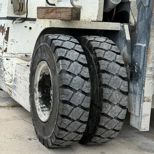 Close-up of heavy-duty dual tires on a construction vehicle with weathered white body and rugged treads.