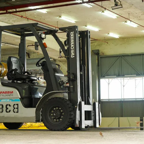 Industrial forklift parked inside a spacious warehouse with concrete floors and large windows providing natural light