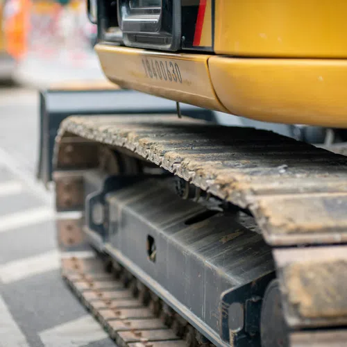 Close-up of a yellow excavator's heavy-duty caterpillar tracks on a construction site road.
