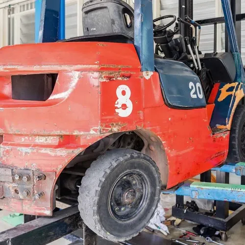 Close-up of a worn red and blue forklift in an industrial workshop during repair or maintenance work