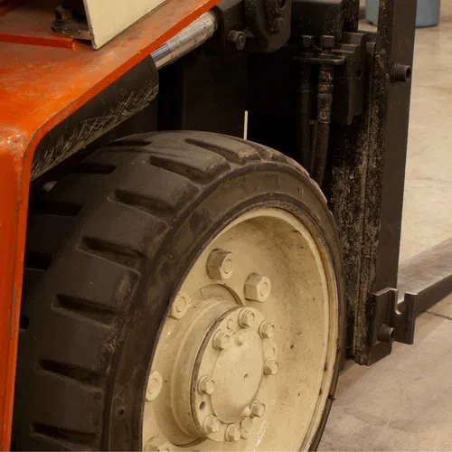Close-up of a forklift tire and part of the lifting mechanism on a warehouse floor.