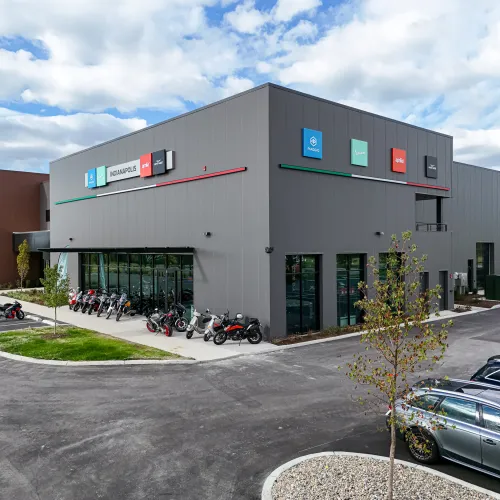 Modern gray motorcycle dealership building with multiple motorbikes displayed outside under a blue sky with clouds.