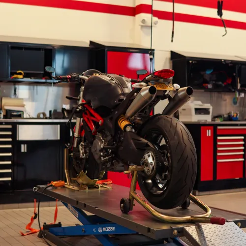 Ducati motorcycle on a blue lift in a garage with red and black tool cabinets and red stripes on the wall.