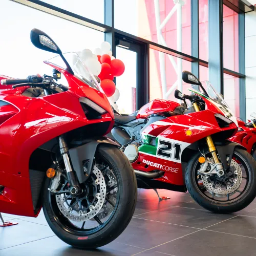 Three red Ducati sport motorcycles displayed indoors with clear showroom windows and balloons in the background