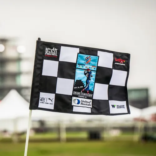 Black and white checkered flag with golf tournament logos and sponsors in outdoor blurred background.
