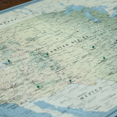 Close-up photo of a North America map showing United States, Canada, and Mexico with location pins placed on various cities.
