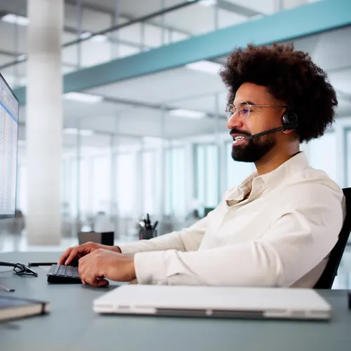 Man wearing headset working on computer in a modern bright office environment