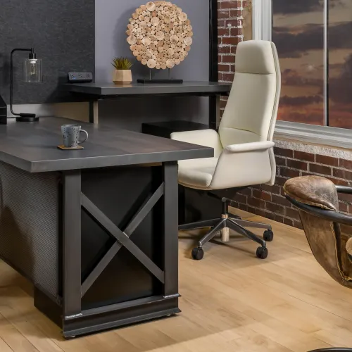 Modern office space with a large dark metal desk, white leather chair, and brown leather seating against brick walls.