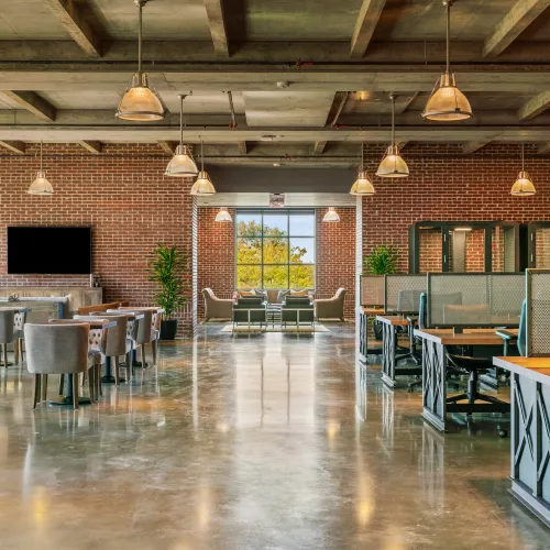 Modern open office space with exposed brick walls, large windows, and industrial ceiling lighting.