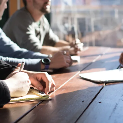 a group of people sitting at a table writing on paper