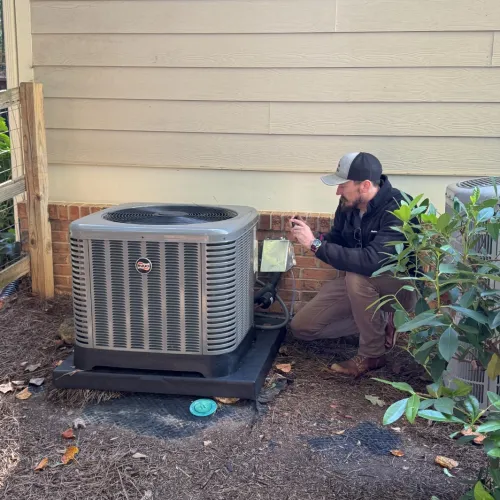 Technician inspecting and repairing an outdoor air conditioning unit beside a house with surrounding greenery.
