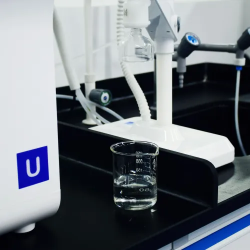 Clear beaker with liquid on black lab countertop near white lab equipment and faucets in modern laboratory.