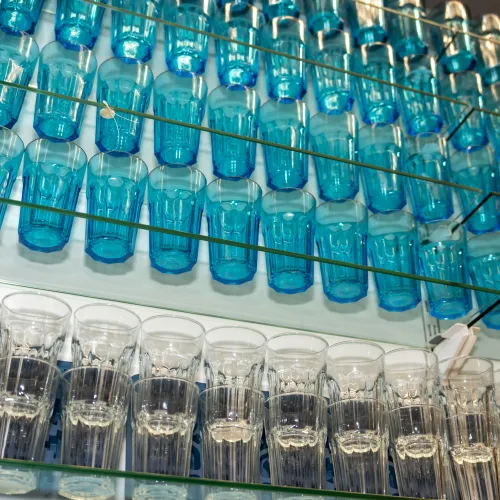 Rows of blue and clear glass cups neatly arranged on glass shelves against a white wall.