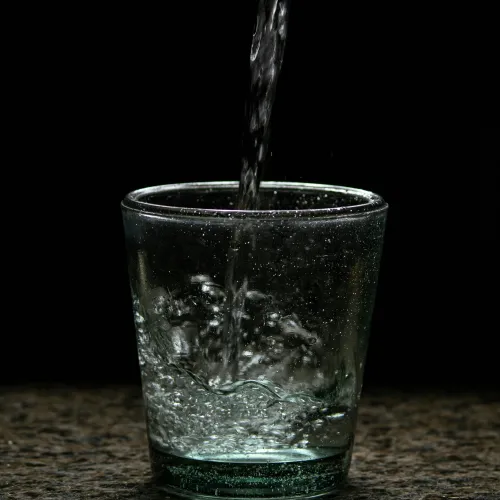 Clear water pouring into a transparent glass with bubbles against a dark background.