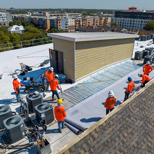 Mattco Roofing and Construction crew installing TPO single-ply roofing membrane on commercial flat roof in Austin Texas
