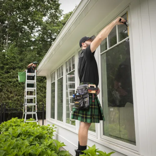 a man in a kilt standing on a ladder outside a house