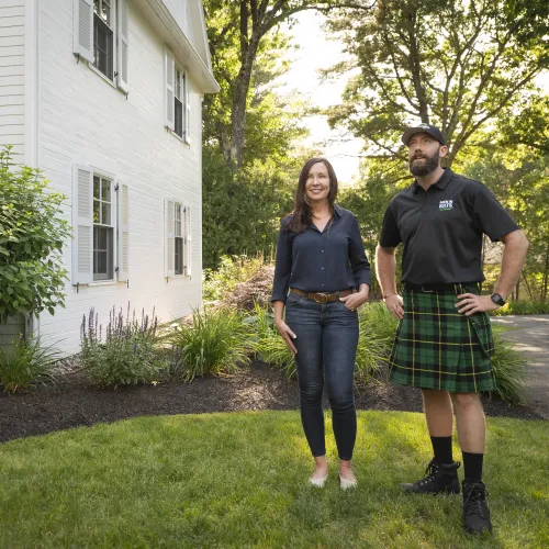 a man and woman standing in a yard with a house and trees
