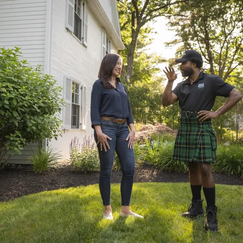 a man and woman standing in a yard with a house and trees