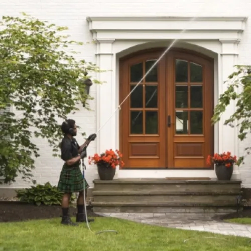 a person in a kilt holding a cane in front of a house