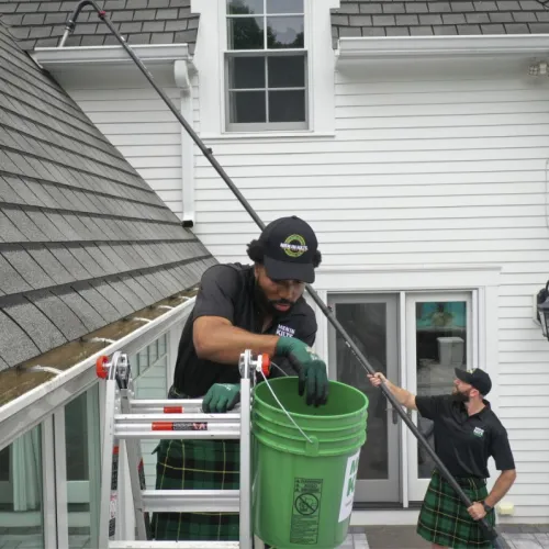 a couple of men in black hats and green gloves working on a green garbage can