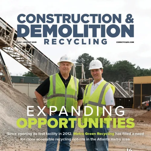 Two construction workers in hard hats and safety vests standing at a recycling facility construction site.