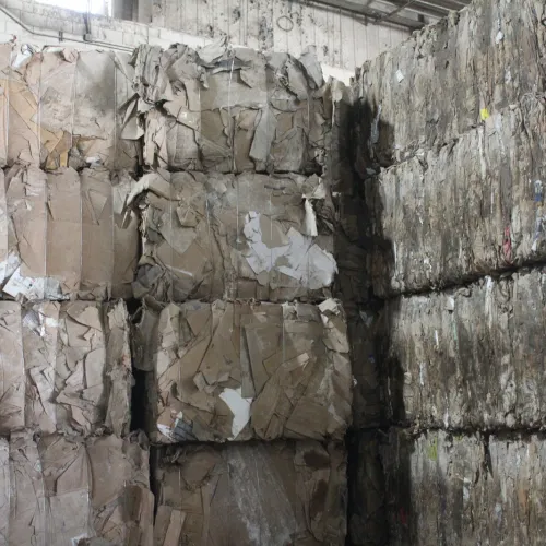 Stacks of compacted recycled cardboard bales in an industrial warehouse ready for processing or shipping.