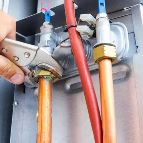 Hand tightening a pipe fitting on copper plumbing with an adjustable wrench, surrounded by pipes and valves