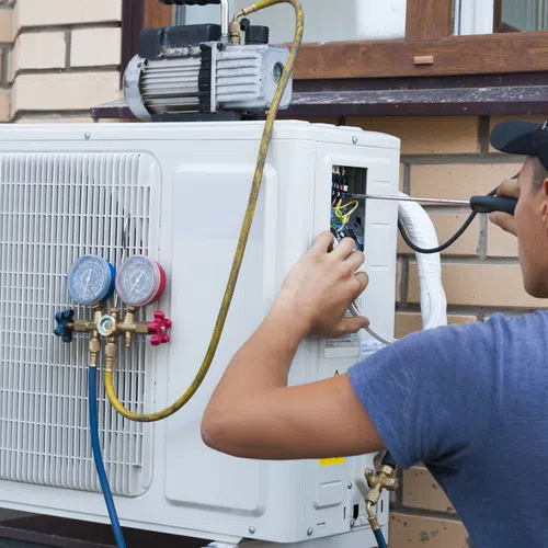 Technician repairing an air conditioning unit on a brick wall, showcasing tools and gauges.
