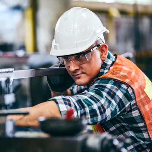 Two construction workers in helmets and vests operating machinery in an industrial warehouse setting.