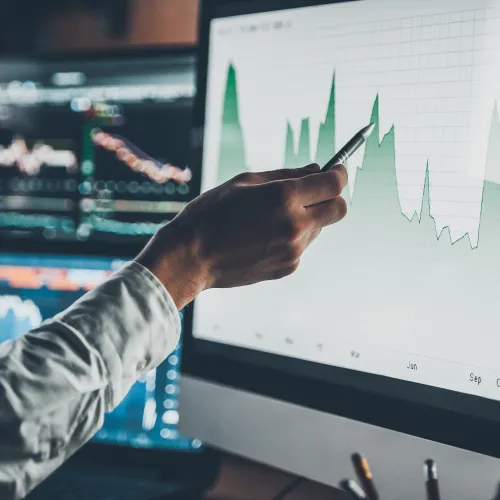 Person analyzing financial growth charts on computer screens with graphs and data points in an office setting