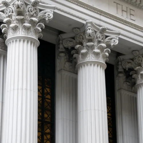 Close-up of classical white stone columns with ornate capitals outside a bank building.
