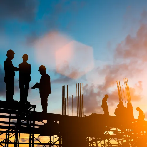 Silhouettes of construction workers on scaffolding against a glowing sunset sky with clouds.