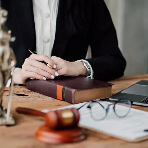 Legal professional sitting at desk with law book, gavel, scales of justice, laptop, and documents.
