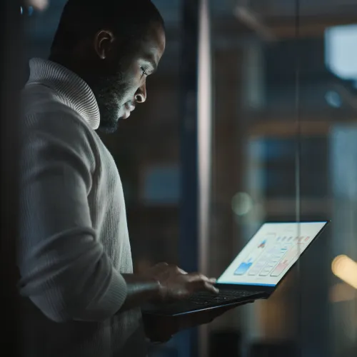 Man in a turtleneck working on a laptop in a dimly lit office at night