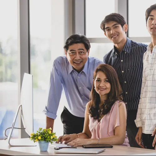 Four people posing confidently around a desk with a computer in a bright modern office environment
