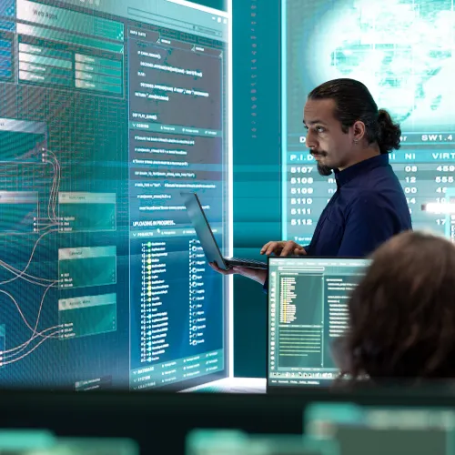 IT professionals analyzing complex data visualizations and code on multiple large screens in a modern control room.