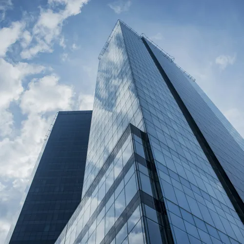 Modern glass skyscraper reflecting clouds against a blue sky in an urban setting.