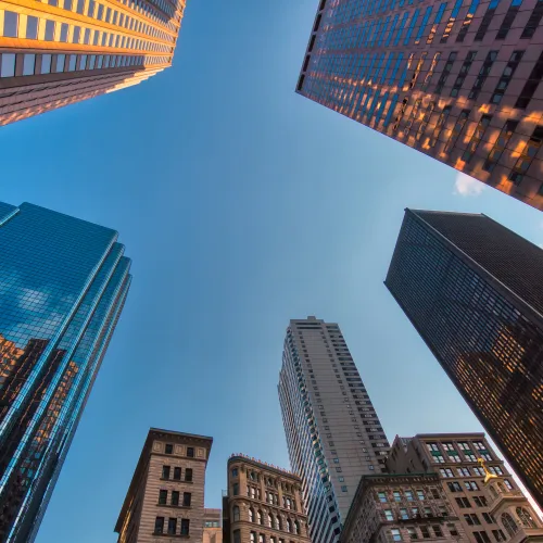 Looking up at diverse skyscrapers surrounding a clear blue sky in a city downtown during sunset.