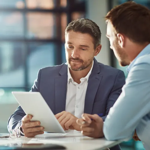 Two businessmen in office discussing work using a digital tablet during a meeting.