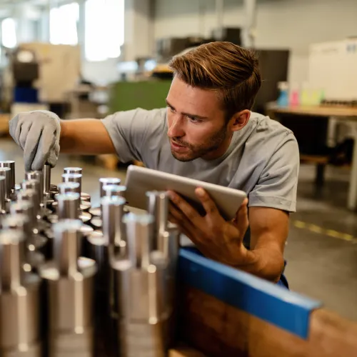 Engineer inspecting metal parts in factory while holding digital tablet during quality control process