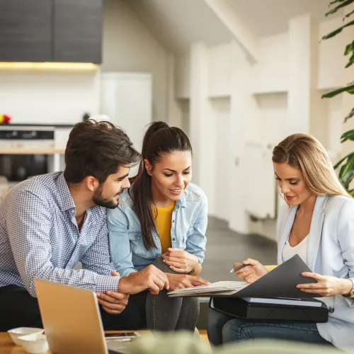 Couple consulting a female agent with documents in a modern living room setting during a financial meeting.
