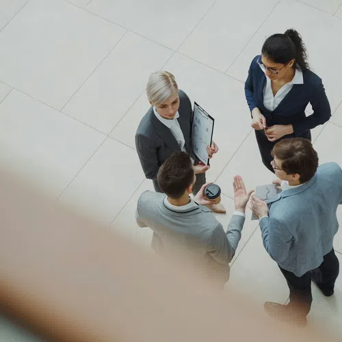 Overhead view of four business professionals in a meeting discussing documents in a modern office space.