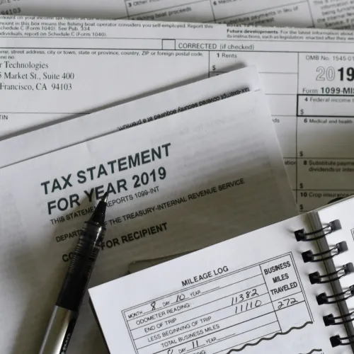 2019 tax statement, IRS forms, and a mileage logbook with pen on top of paperwork.