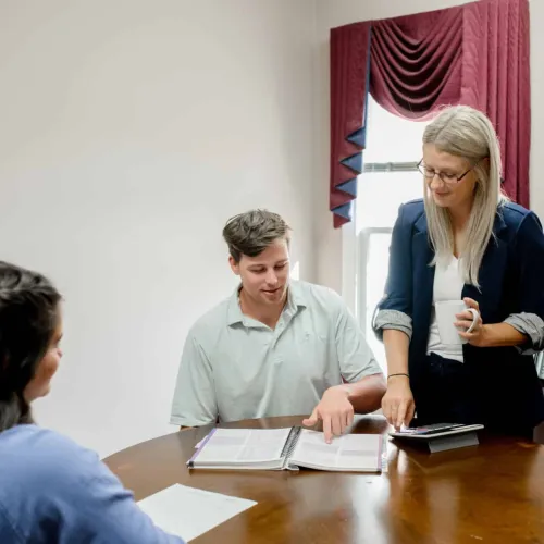 Three people collaborating around a table with documents and a tablet in a brightly lit office room.