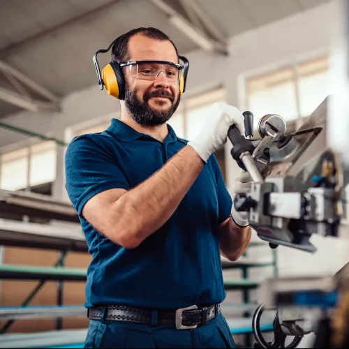 Manufacturing worker wearing safety gear operates industrial machinery in a factory setting with focused expression